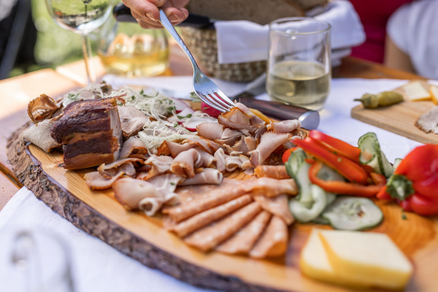 Angerichtete Jause im Gastgarten in der Erlachmühle am Mondsee im Salzkammergut, auf einem Holzbrett liegen Gemüse, Käse und Fleisch.